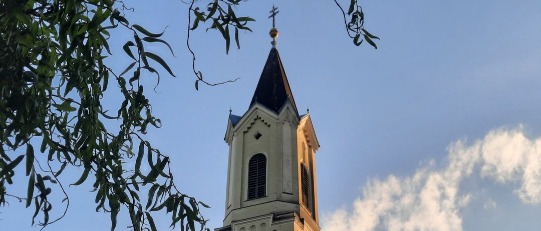 Ein hoher Kirchturm mit einer Uhr und einer Fahne mit einer Maske darauf.