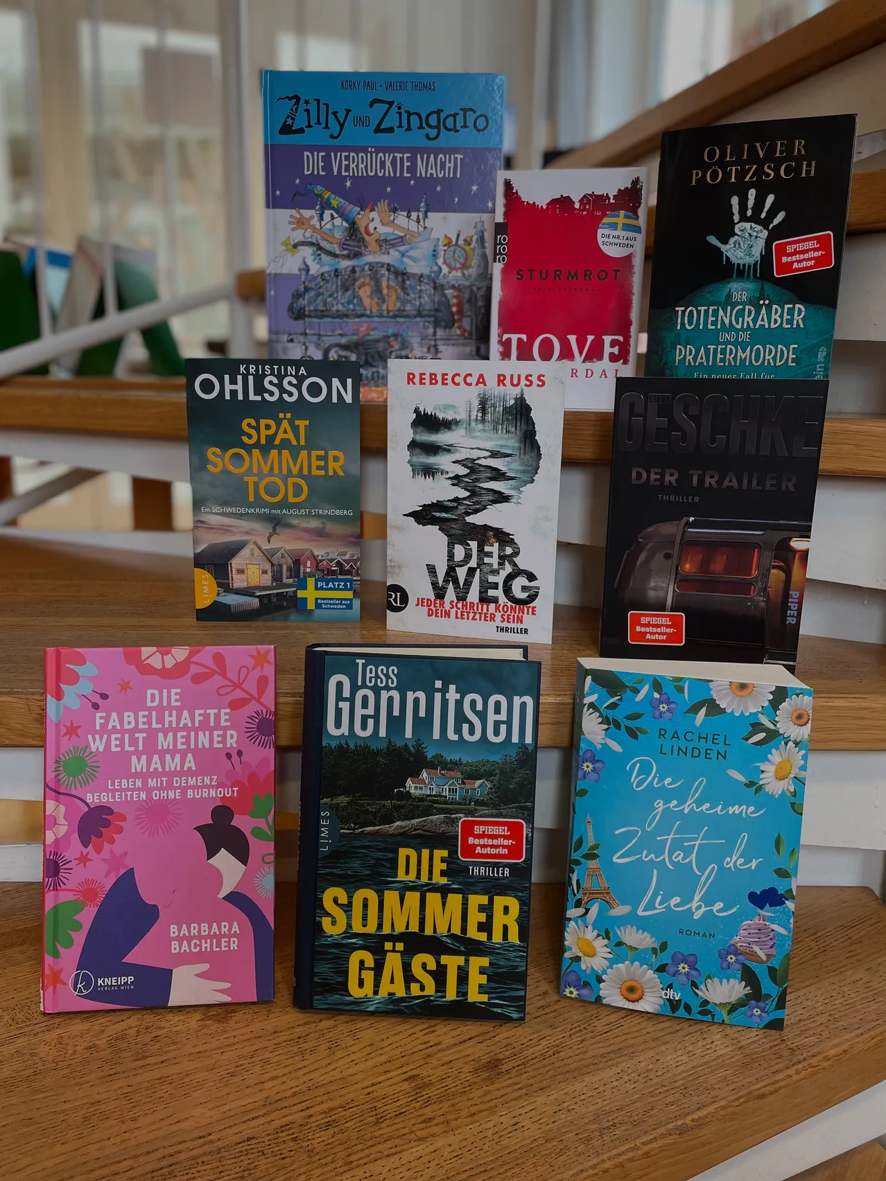 Eine Sammlung von Büchern auf einer Holztreppe, darunter Titel wie 'Die Verrückte Nacht', 'Der Weg', 'Geschak' und 'Die Sommer Gaste'.