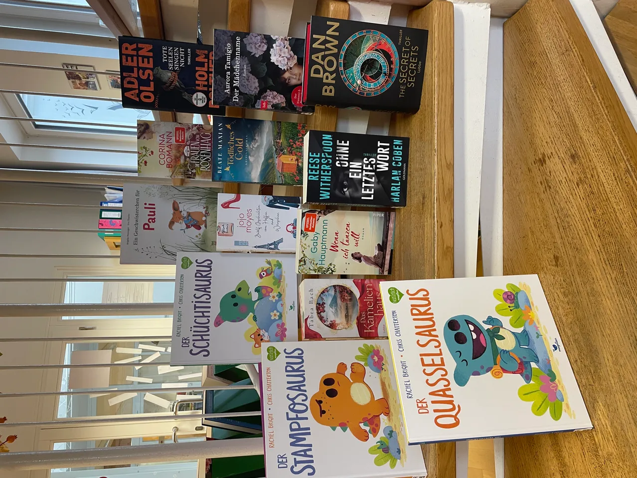 Ein Holzregal mit aufgereihten Büchern, darunter Titel wie Quasselsaurus, Stamposaurus und Die Geheimnisse des Universums.