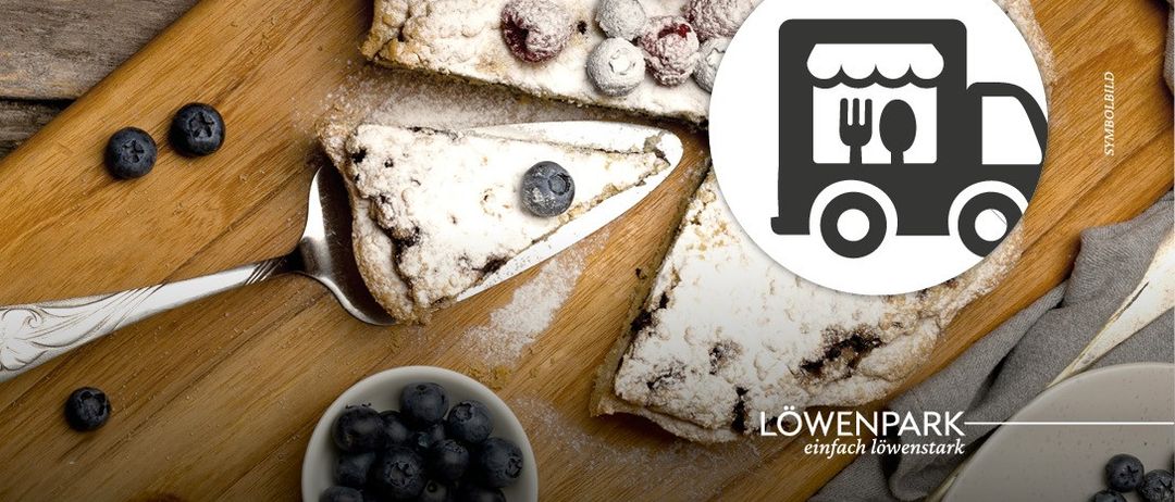 Ein Holzschneidebrett mit einem Stück Blaubeerkuchen, einem silbernen Messer und einer Schüssel mit Blaubeeren. Das Bild ist in einem kreisförmigen Rahmen mit einem LKW-Logo.