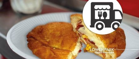 Ein Halb aufgegessenes Sandwich auf einem weißen Teller, mit einem Eimer-Symbol darauf, wahrscheinlich von einem Food Truck, mit dem Namen Loewenpark darauf.