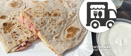 A half-eaten sandwich with ham and cheese on a white plate, next to a bowl of white sauce. An image of a food truck with utensils is also visible.