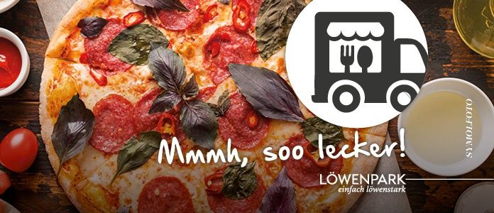 Eine Pizza mit Peperoni, Basilikumblättern und roten Paprikaschoten auf einem Holztisch mit einer Schüssel Sauce und einem LKW-Logo.