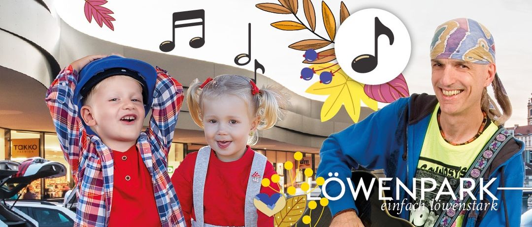 Ein Mann spielt Gitarre mit einem Jungen und einem Mädchen vor ihm, umgeben von Noten und Blättern. Der Mann lächelt und die Kinder schauen in die Kamera.