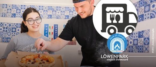 A man and a woman are standing in front of a wall with blue tiles, smiling and holding a pizza box. The man is wearing a black shirt and the woman is wearing glasses. The pizza box has a pizza with black olives. There is a logo in the middle of the image.