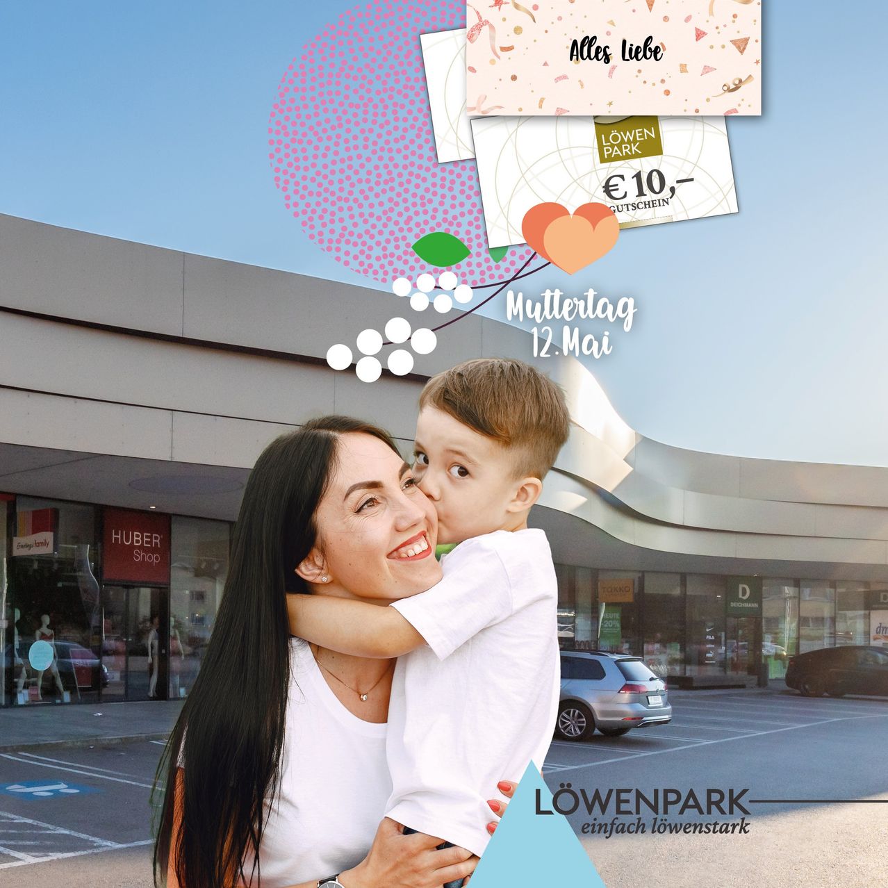 Eine Frau, die einen kleinen Jungen vor einem Einkaufszentrum hält, mit einem 10-Euro-Gutschein, der über ihnen schwebt. Der Gutschein sagt 'Alles Liebe'. Ein Auto ist im Hintergrund geparkt.