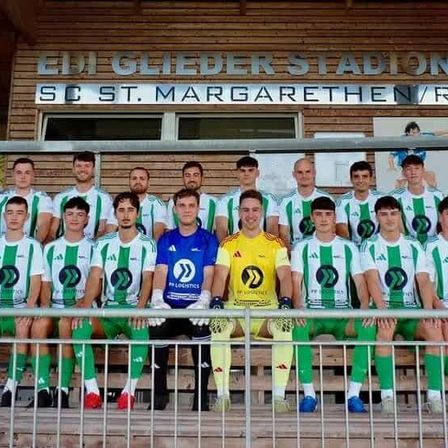 Eine Fußballmannschaft posiert für ein Foto vor dem Edi Glieder Stadion, wobei die Spieler grüne und weiße Trikots tragen.