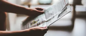 Die Hände einer Person halten eine Zeitung mit einer Anzeige, möglicherweise vor einem unscharfen Hintergrund.