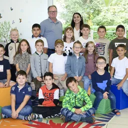 Eine Gruppe von Kindern und zwei Erwachsenen posiert für ein Foto in einem Raum mit bunten Kissen und einer Schmetterlingswanddekoration.