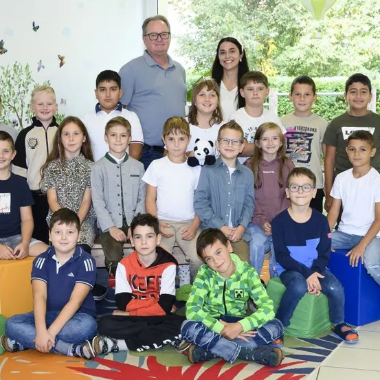 Eine Gruppe von Kindern und zwei Erwachsenen posiert für ein Foto in einem Raum mit bunten Kissen und einer Schmetterlingswanddekoration.
