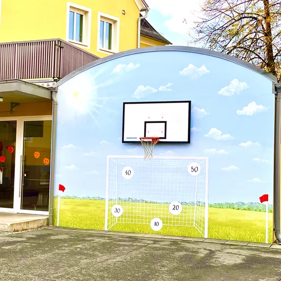 Ein gelbes Gebäude mit Glastüren und Fenstern hat einen Basketballkorb, der auf einer Wand gemalt ist. Der Korb ist von Zahlen umgeben, die die Wurfweiten anzeigen.