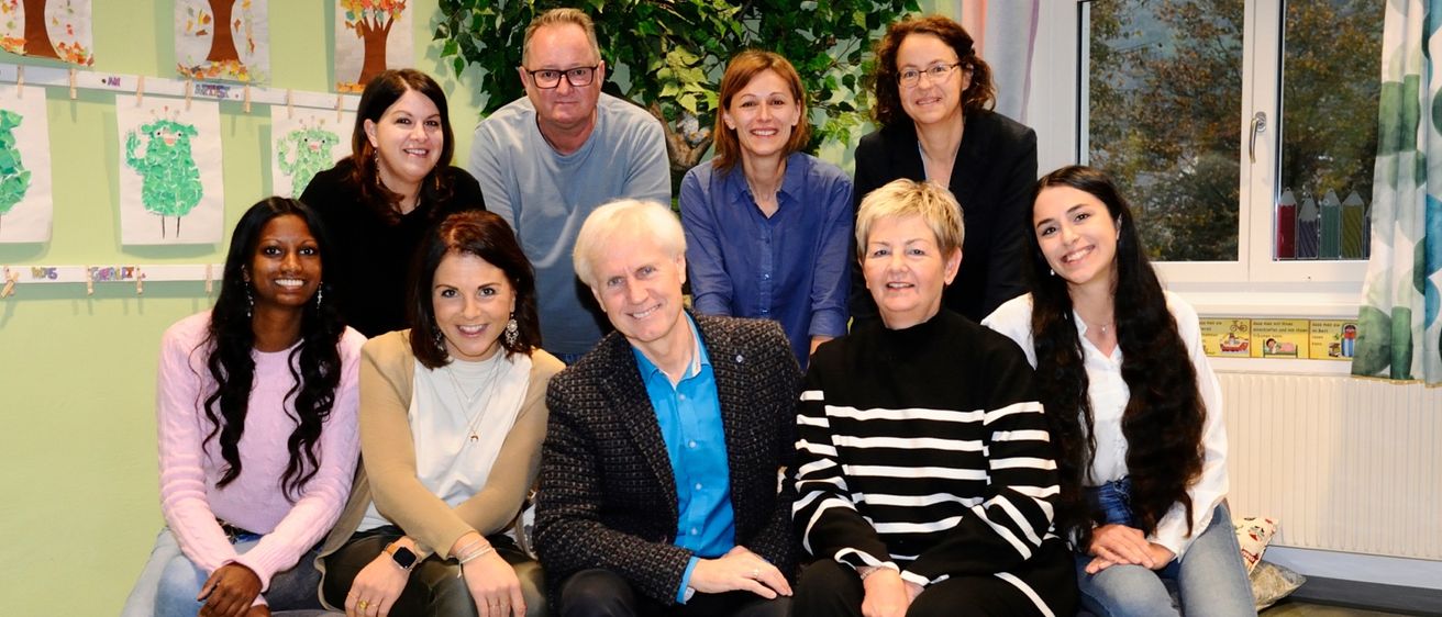 Eine Gruppe lächelnder Erwachsener, einschließlich Männer und Frauen, posiert für ein Foto mit einer grünen Pflanze im Hintergrund.