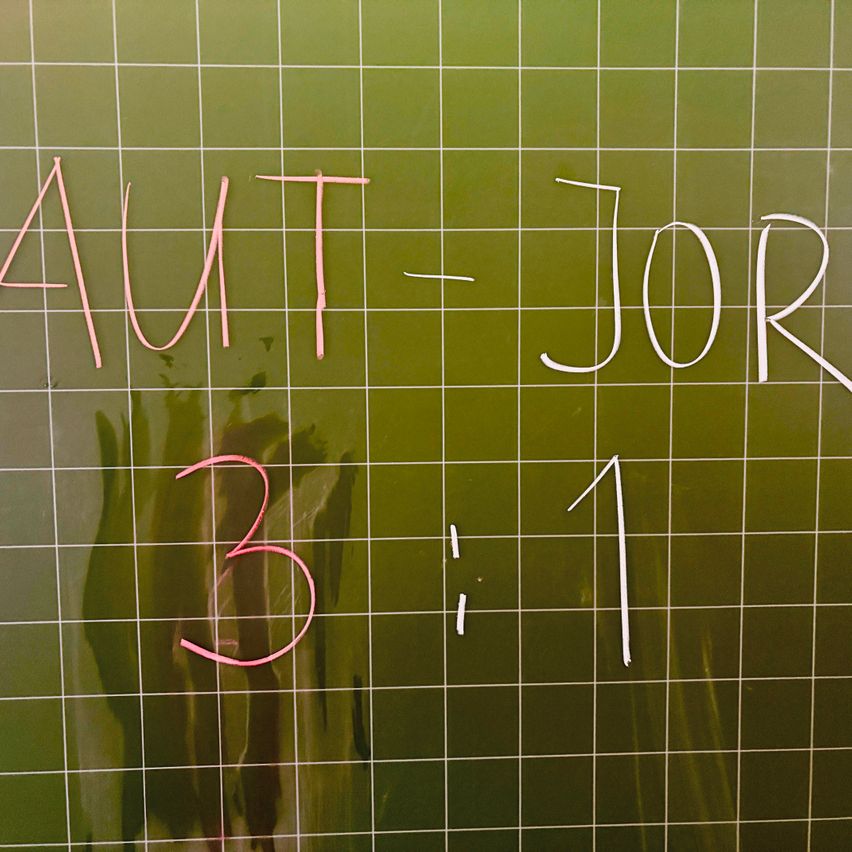 Ein grüner Gitterhintergrund mit 'AUT' und '3' in Pink sowie '- JOR' und '1' in Weiß. Das Raster ist gleichmäßig abgestanden.