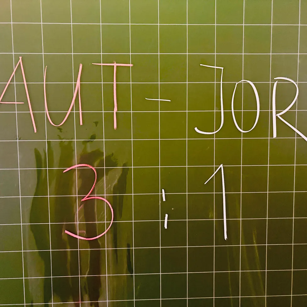 Ein grüner Gitterhintergrund mit 'AUT' und '3' in Pink sowie '- JOR' und '1' in Weiß. Das Raster ist gleichmäßig abgestanden.