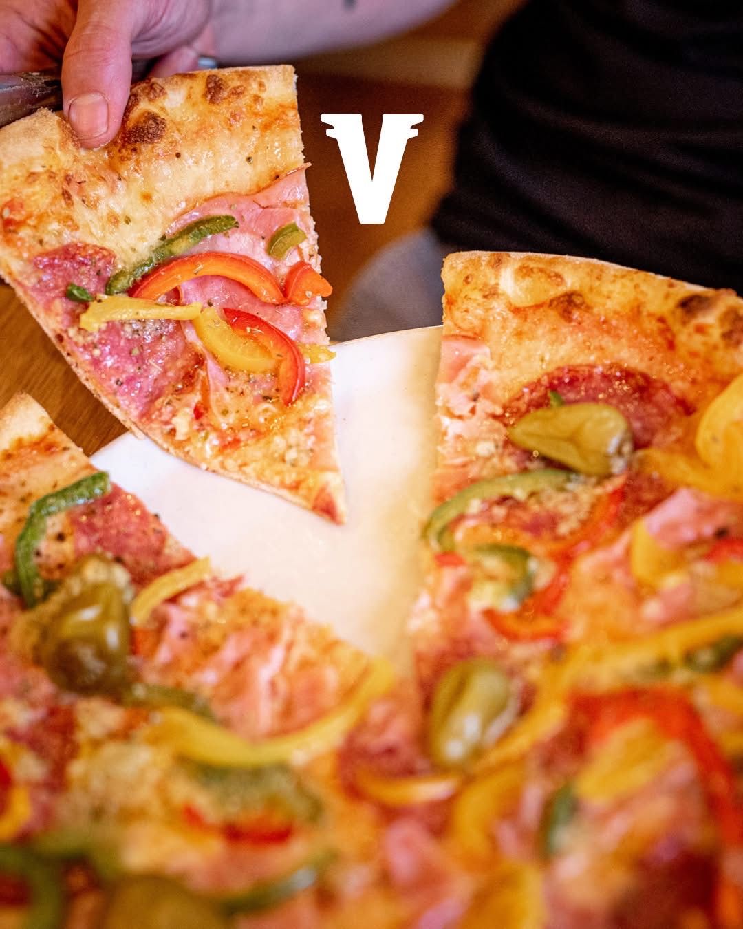 Eine Nahaufnahme eines Pizzastücks mit Toppings wie Paprika, Schinken und Käse. Das Stück wird von einer Person gehalten.