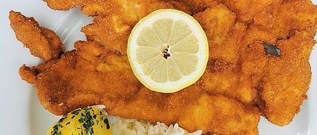 Ein Teller mit gebratenem Fisch, einer Zitronenscheibe und Reis mit Beilage, auf einem weißen Teller serviert.