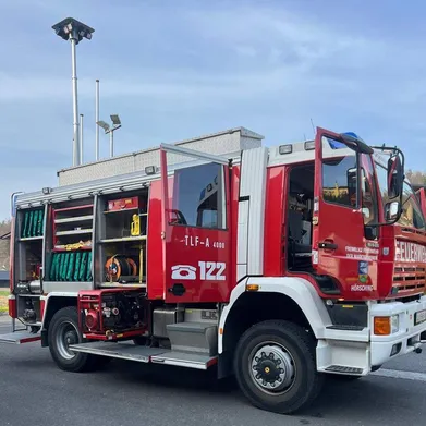 Ein roter Feuerwehrwagen ist vor einem Gebäude mit offenen Türen geparkt.