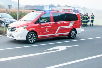 Ein rotes Feuerwehrfahrzeug fährt auf der Straße, im Hintergrund ist ein Krankenwagen zu sehen.