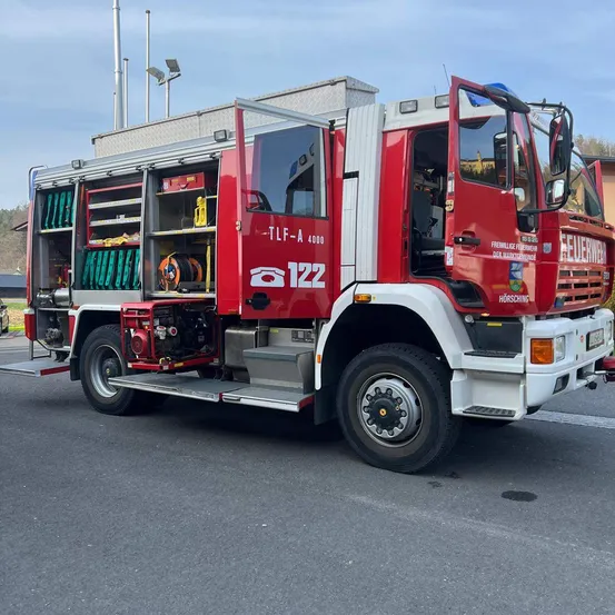Ein roter Feuerwehrwagen steht mit offenen Türen am Straßenrand.