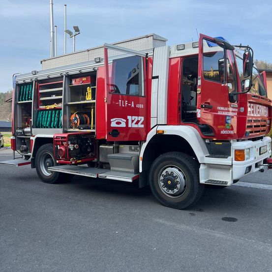 Ein roter Feuerwehrwagen steht mit offenen Türen am Straßenrand.