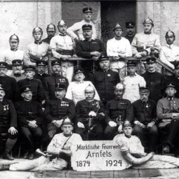 Ein Schwarz-Weiß-Foto einer Gruppe von Feuerwehrleuten in Uniform, einige sitzend und andere stehend, posieren für ein Foto.