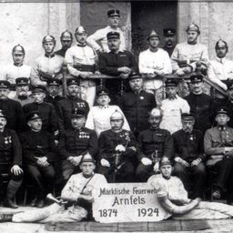 Ein Schwarz-Weiß-Foto einer Gruppe von Feuerwehrleuten in Uniform, einige sitzend und andere stehend, posieren für ein Foto.