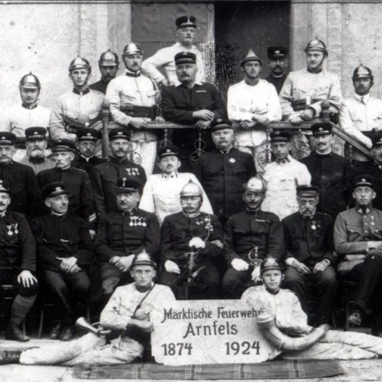 Ein Schwarz-Weiß-Foto einer Gruppe von Feuerwehrleuten in Uniform, einige sitzend und andere stehend, posieren für ein Foto.