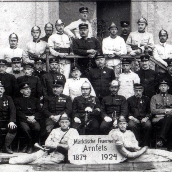 Ein Schwarz-Weiß-Foto einer Gruppe von Feuerwehrleuten in Uniform, einige sitzend und andere stehend, posieren für ein Foto.