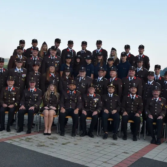 Eine Gruppenaufnahme von uniformierten Beamten, darunter sowohl Männer als auch Frauen, die auf einem gepflasterten Weg posieren. Sie tragen Hüte und viele haben Medaillen an ihren Uniformen.