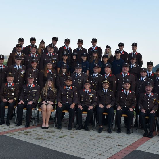 Eine Gruppenaufnahme von uniformierten Beamten, darunter sowohl Männer als auch Frauen, die auf einem gepflasterten Weg posieren. Sie tragen Hüte und viele haben Medaillen an ihren Uniformen.