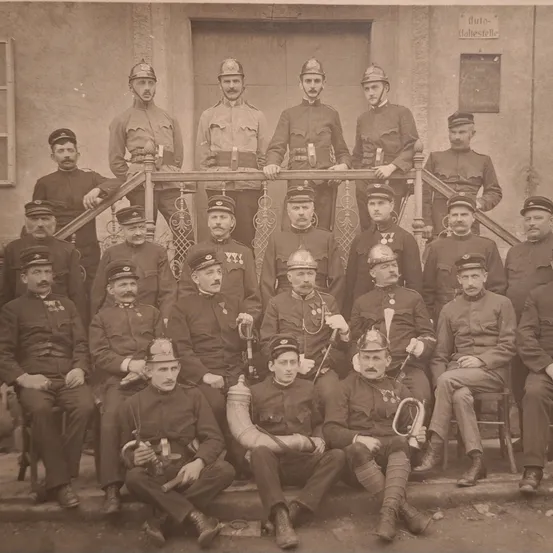 Ein altes Foto einer Gruppe von Militärmännern in Uniform, einige sitzend und andere stehend, mit verschiedenen Mützen und Instrumenten in der Hand.