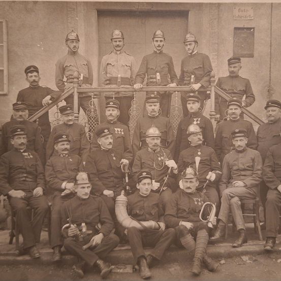 Ein altes Foto einer Gruppe von Militärmännern in Uniform, einige sitzend und andere stehend, mit verschiedenen Mützen und Instrumenten in der Hand.