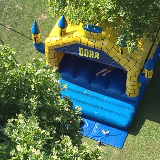 Eine Draufsicht auf ein blaues und gelbes aufblasbares Schloss mit dem Wort DDRR darauf. Eine Person ist drinnen und Schuhe liegen draußen auf dem Boden.