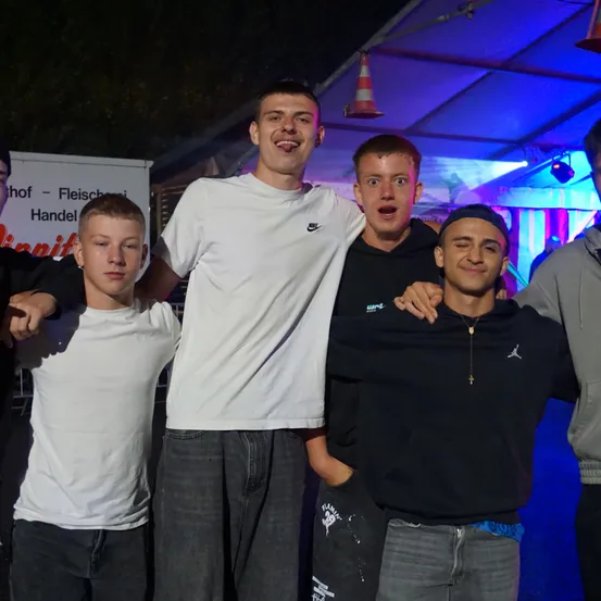 Fünf junge Männer stehen nachts zusammen unter einem Zelt, lächeln und posieren für ein Foto.