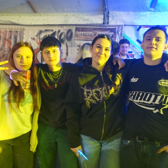 Vier Freunde posieren für ein Foto in einem Club mit Graffiti an der Wand und Neonlichtern.