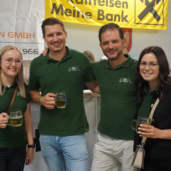 Drei Personen in grünen Poloshirts posieren mit Getränken in den Händen und lächeln vor einem Banner.