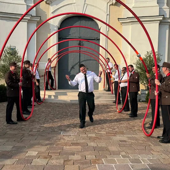 Eine Gruppe uniformierter Personen führt eine koordinierte Aktivität mit roten Rohren vor einem Gebäude durch.