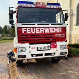 Ein Feuerwehrfahrzeug mit dem Wort Feuerwehr auf der Vorderseite und dem Nummernschild LB 122 FF steht auf einem gepflasterten Weg.
