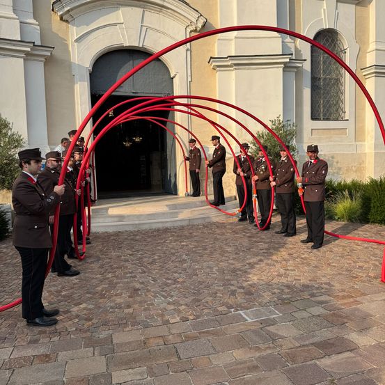 Eine Gruppe uniformierter Personen hält rote Bögen vor einem Gebäude mit einem großen Eingang.