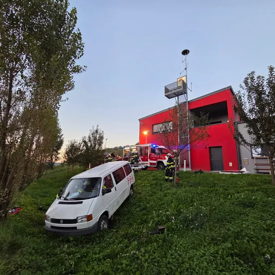 Ein weißer Van ist in ein rotes Gebäude gecrasht, Feuerwehrleute sind am Unfallort.