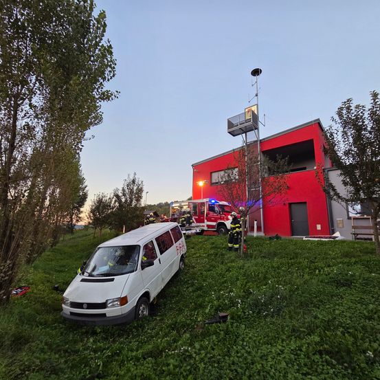 Ein weißer Van ist in ein rotes Gebäude gecrasht, Feuerwehrleute sind am Unfallort.