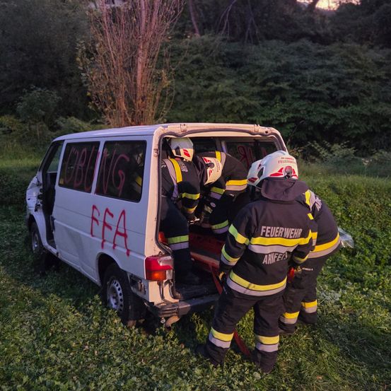 Feuerwehrleute retten eine Person aus einem Van, der im Gras stecken geblieben ist. Darauf steht 'CBUNG FFA'. Sie tragen Helme und Uniformen.