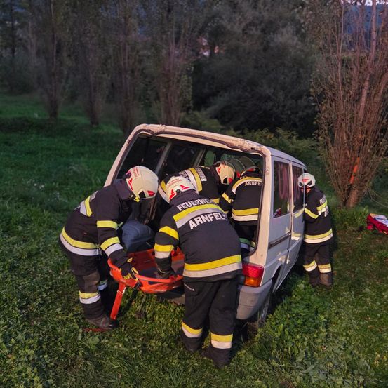 Eine Gruppe Feuerwehrleute steht neben einem beschädigten Van und bereitet sich darauf vor, eine Person mit einer Trage herauszuholen. Sie tragen vollständige Schutzausrüstung.