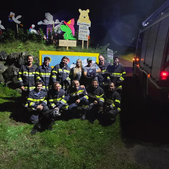 Eine Gruppe von Feuerwehrleuten posiert für ein Foto mit einem Hund vor einer Feuerwache bei Nacht.