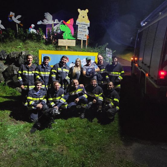 Eine Gruppe von Feuerwehrleuten posiert für ein Foto mit einem Hund vor einer Feuerwache bei Nacht.