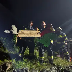 Feuerwehrleute stehen bei Nacht auf einem grasbewachsenen Hügel und halten ein Pappschild mit der Aufschrift 'Elias Sebastian 19.09.2025' mit Dinosaurier- und Vogelausschnitten. Sie tragen Helme und Uniformen.