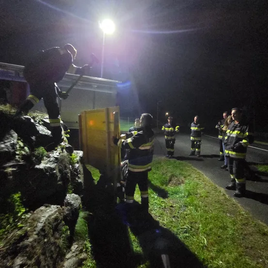 Feuerwehrleute arbeiten bei Nacht an einer Aufgabe, einer mit einem Werkzeug an Felsen. Andere stehen an der Seite.