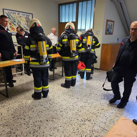 Eine Gruppe von Feuerwehrleuten in Uniform steht in einem Raum mit Tischen und Stühlen. Eine Person hält einen Feuerlöscher.