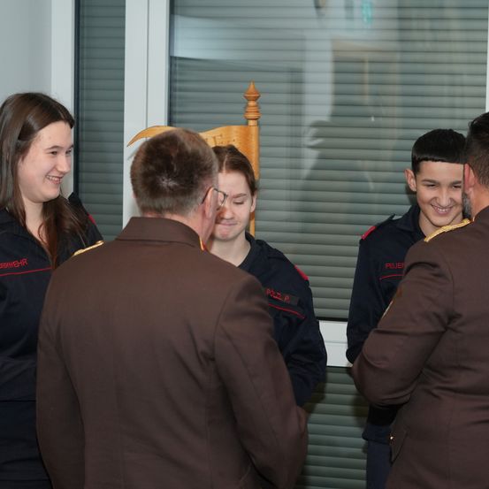 Fünf Menschen in Militäruniformen stehen in einem Raum. Drei sind Frauen, zwei sind Männer. Zwei der Männer tragen eine Brille. Eine Frau lächelt, während sie den Mann vor sich ansieht.