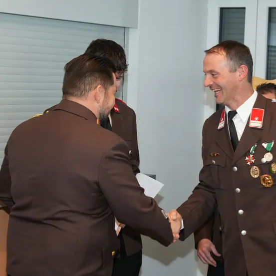 Zwei Männer in Militäruniformen schütteln sich die Hände, lächeln und befinden sich möglicherweise in einem formellen Rahmen.